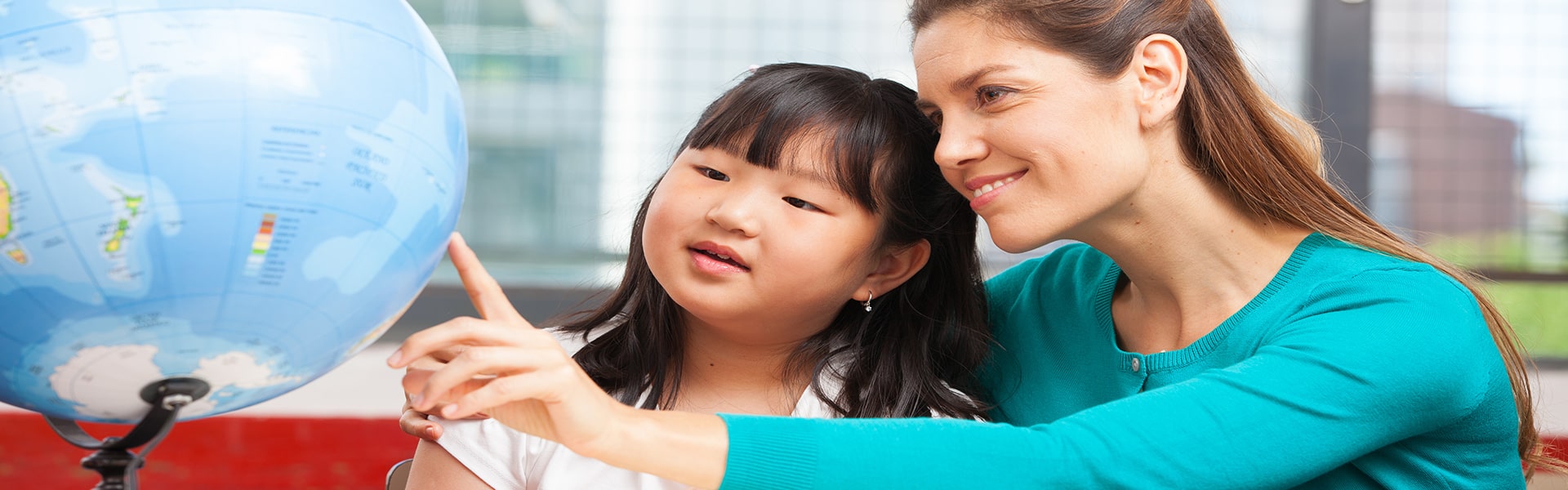 female teacher showing young Asian girl places of a globe of the earth
